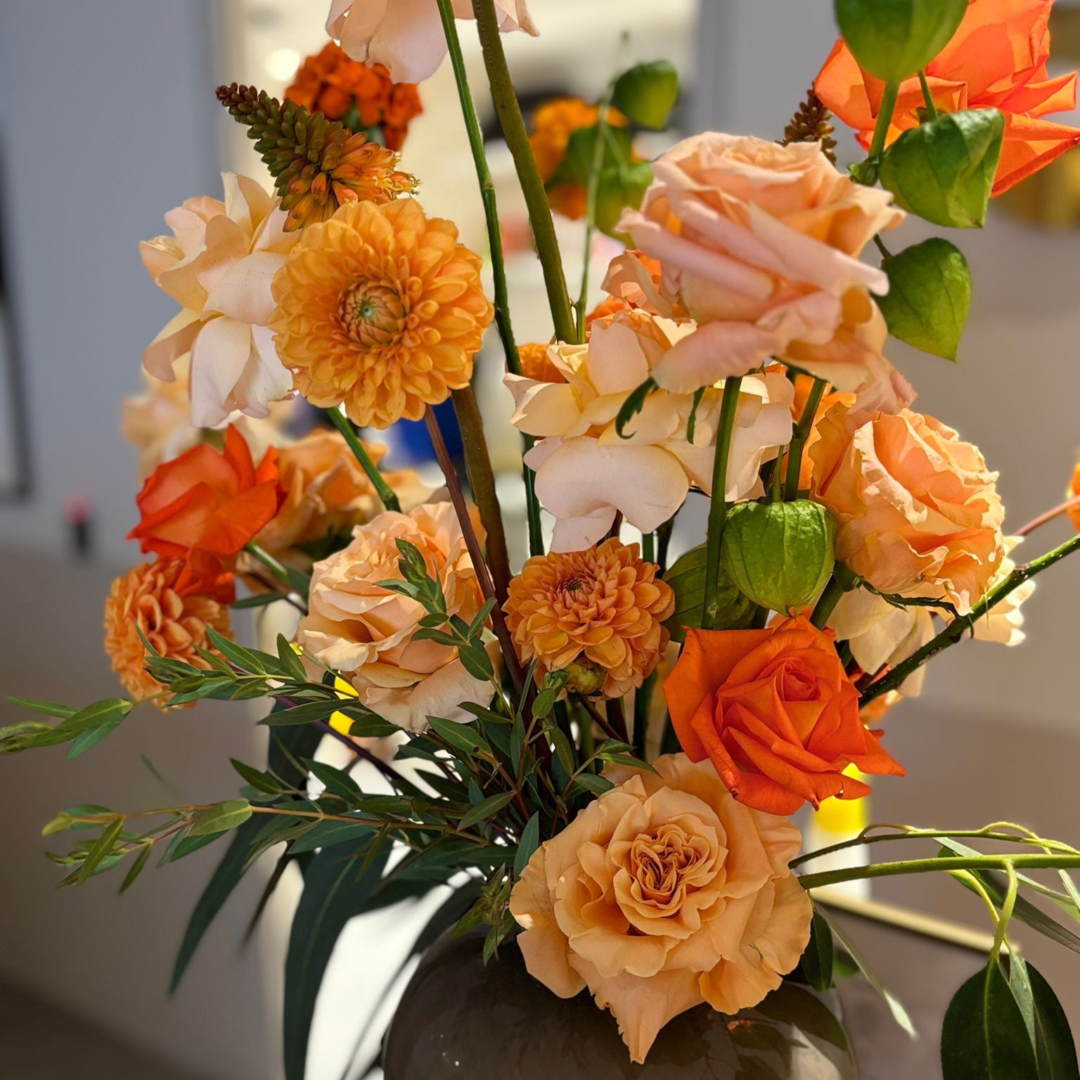 Corporate flowers for an office in Manchester. Orange and peach roses and dahlias in a stone vase in an office setting.