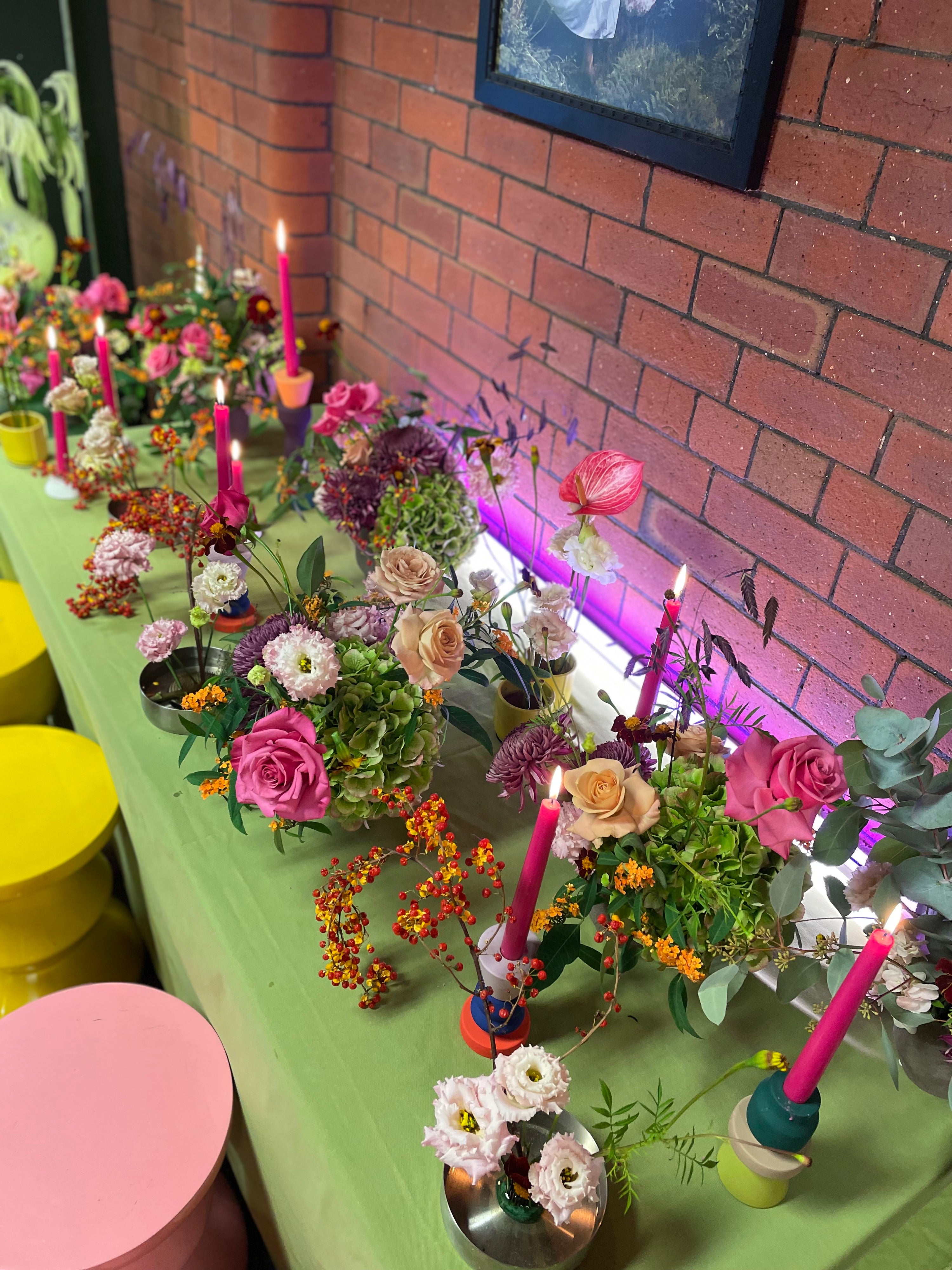 Decorative table setup with flowers, candles, and colorful stands against a brick wall.