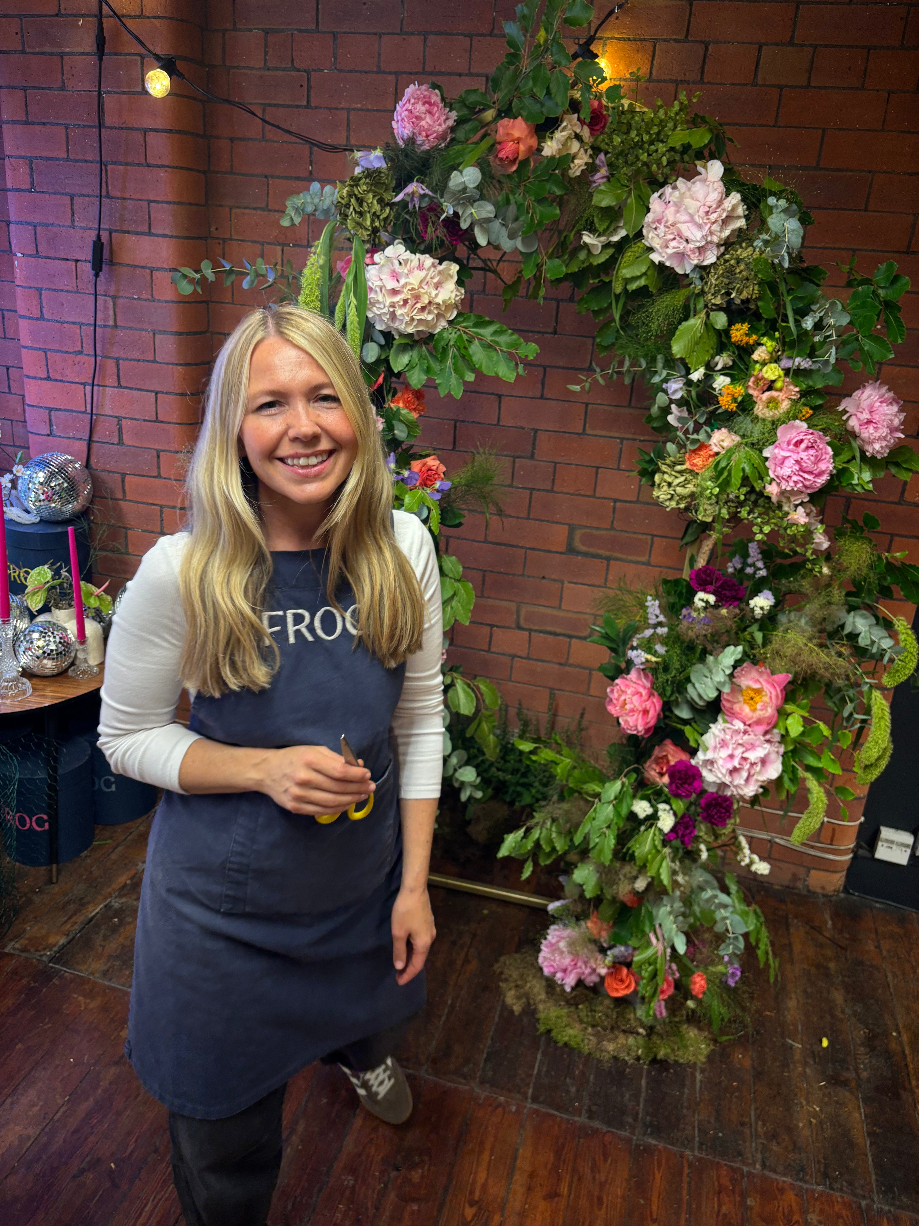 Woman standing in front of a floral archway with a brick wall background