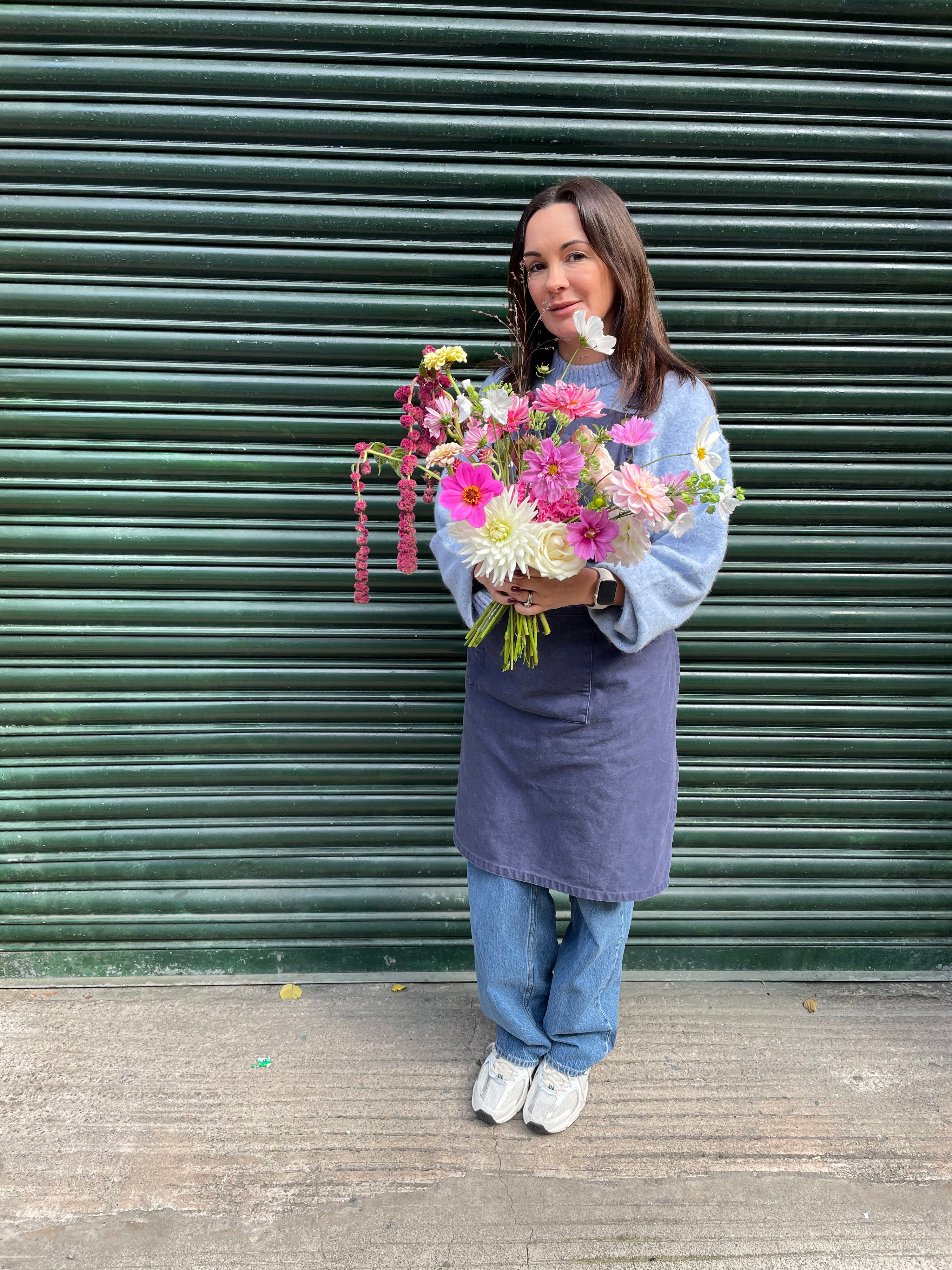 Person holding a bouquet of flowers in front of a green shutter