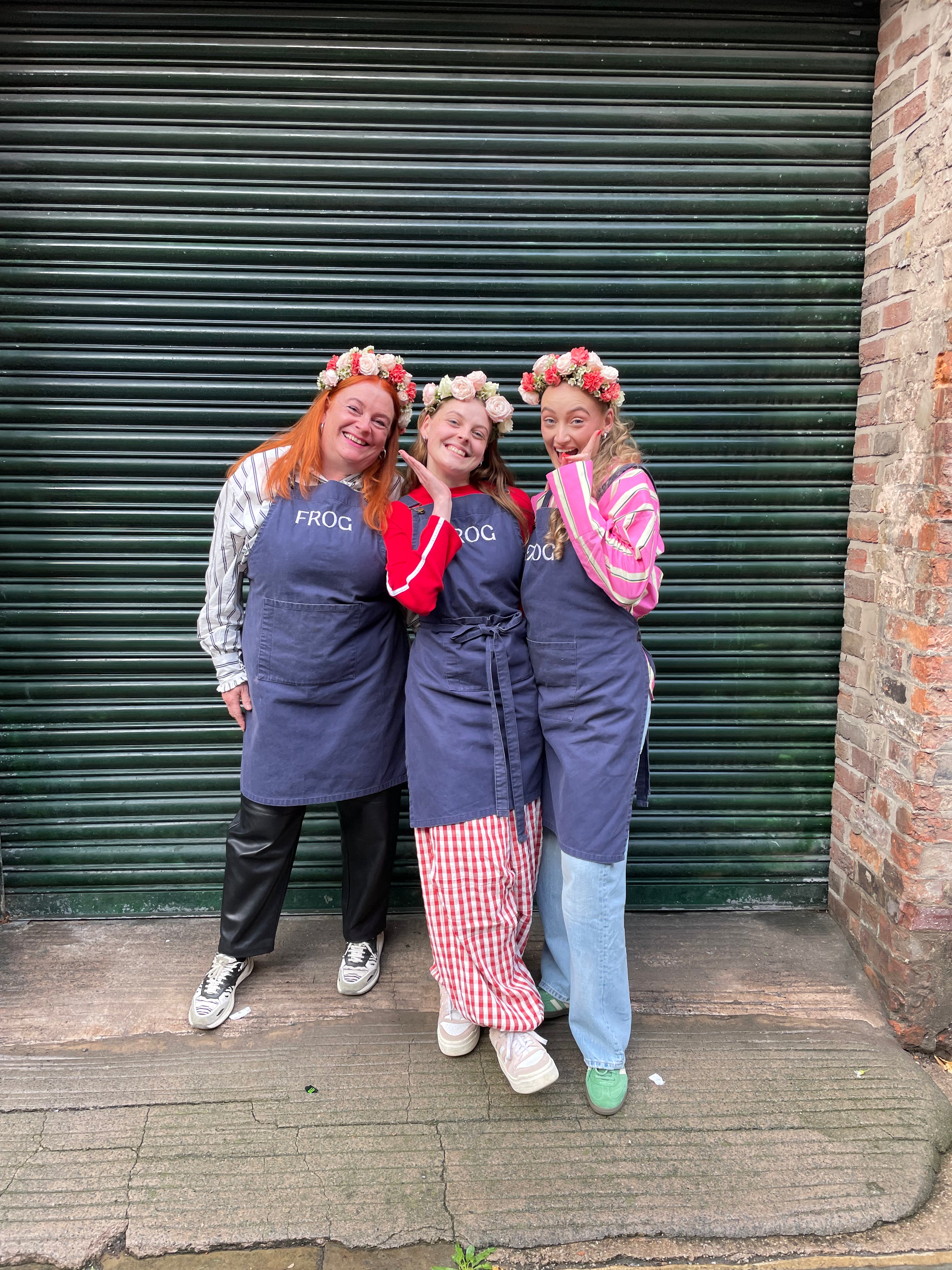 Three women in matching outfits with 'FROG' branding standing in front of a closed shutter.
