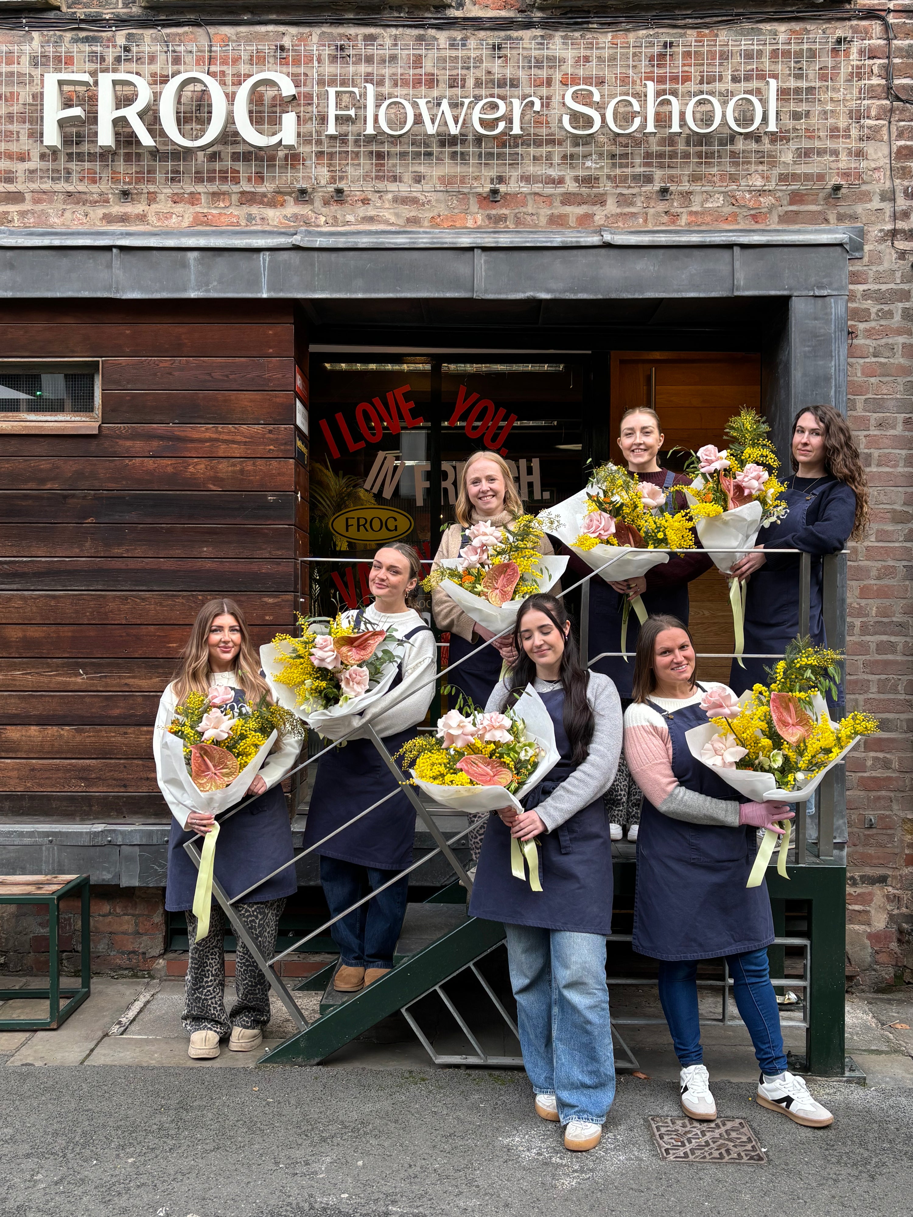 Group of people holding flower bouquets in front of FROG Flower School.