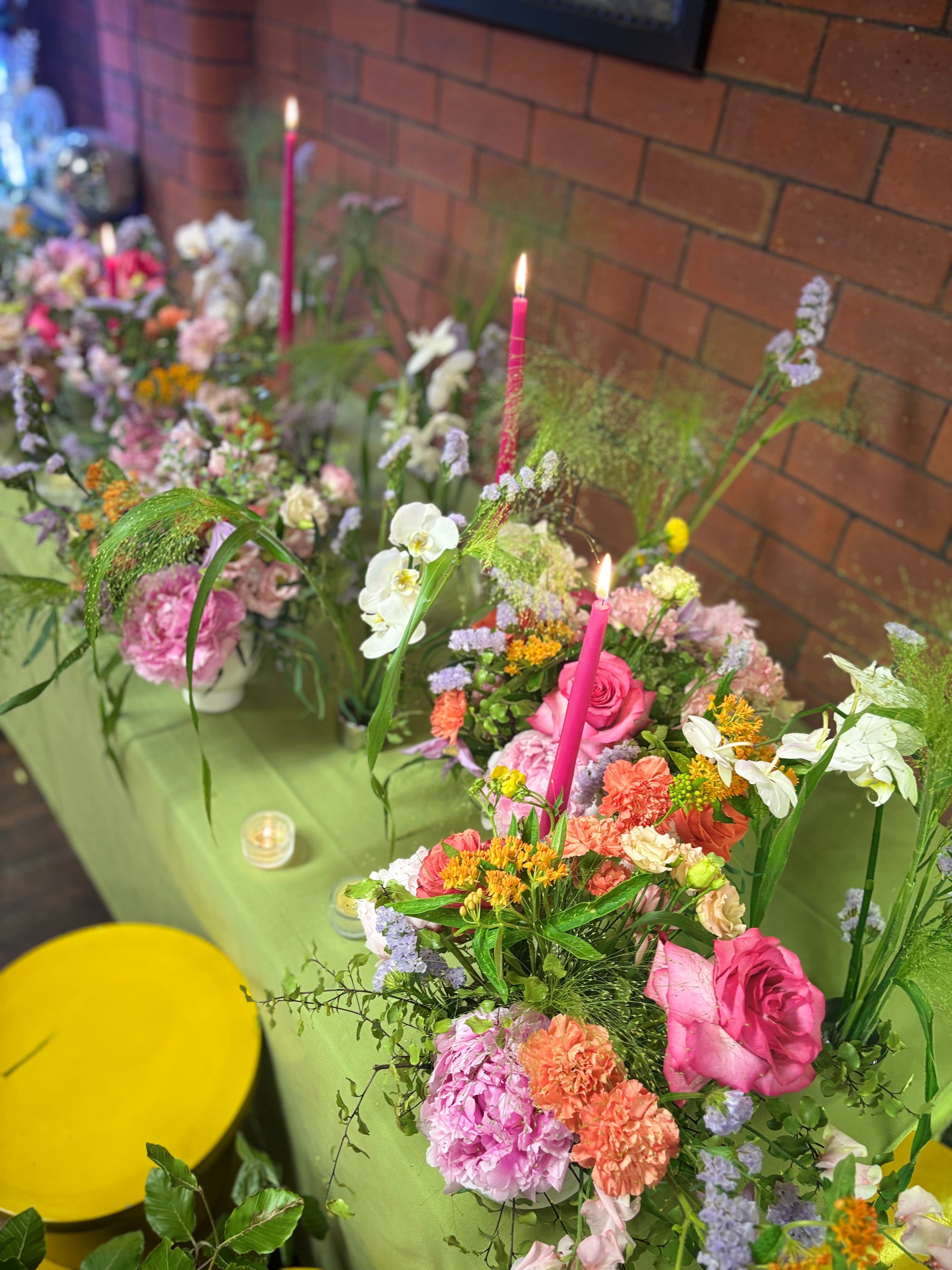Decorative table with flowers, candles, and a green chair against a brick wall.