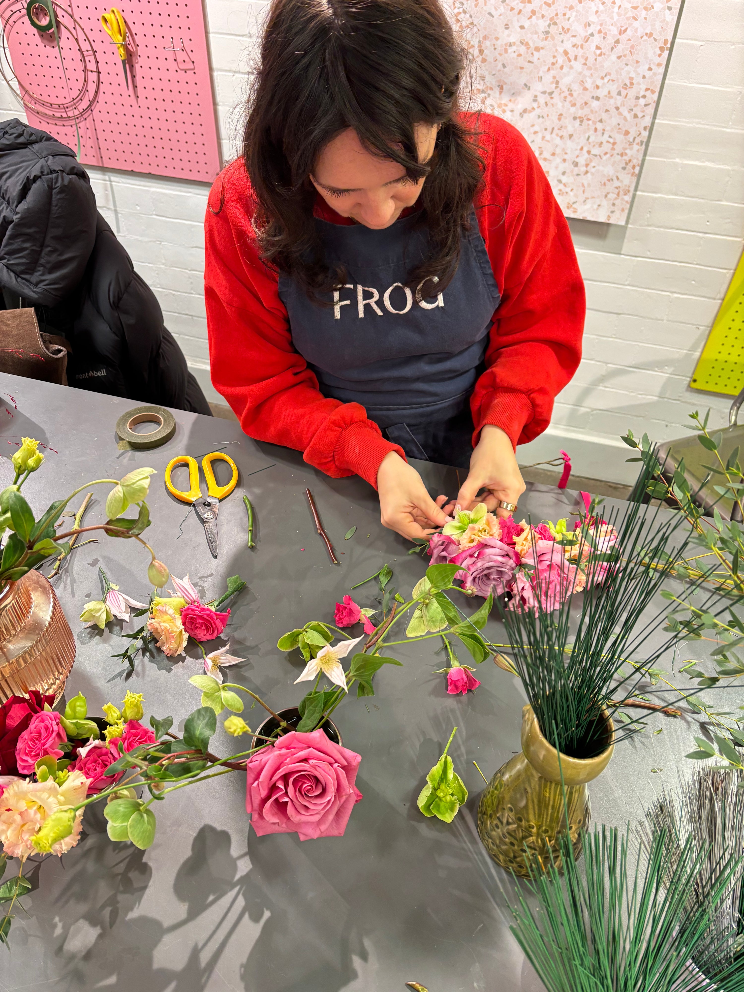 Person arranging flowers on a table with various floral materials and tools.