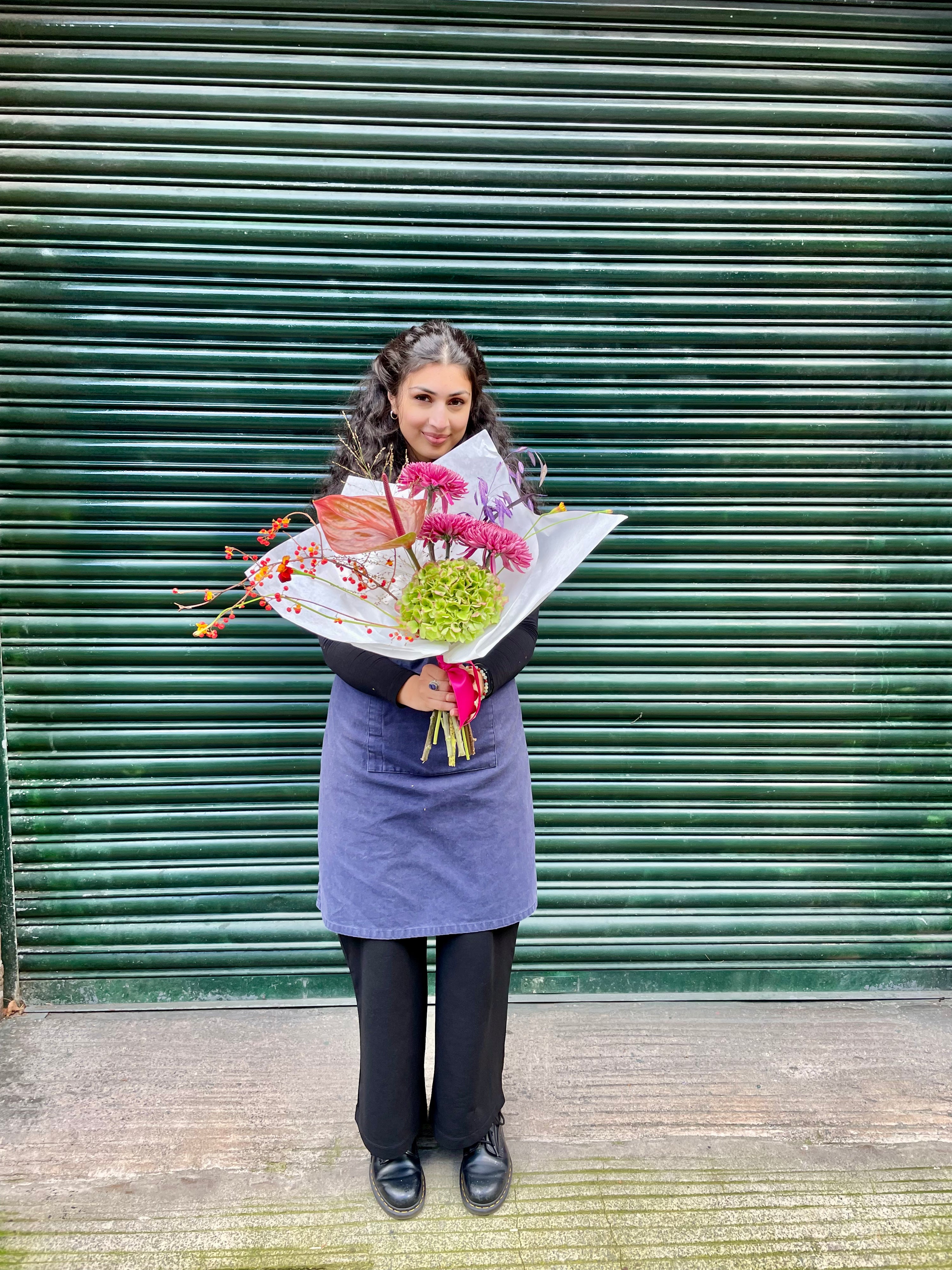 Person holding a bouquet of flowers in front of a green shutter