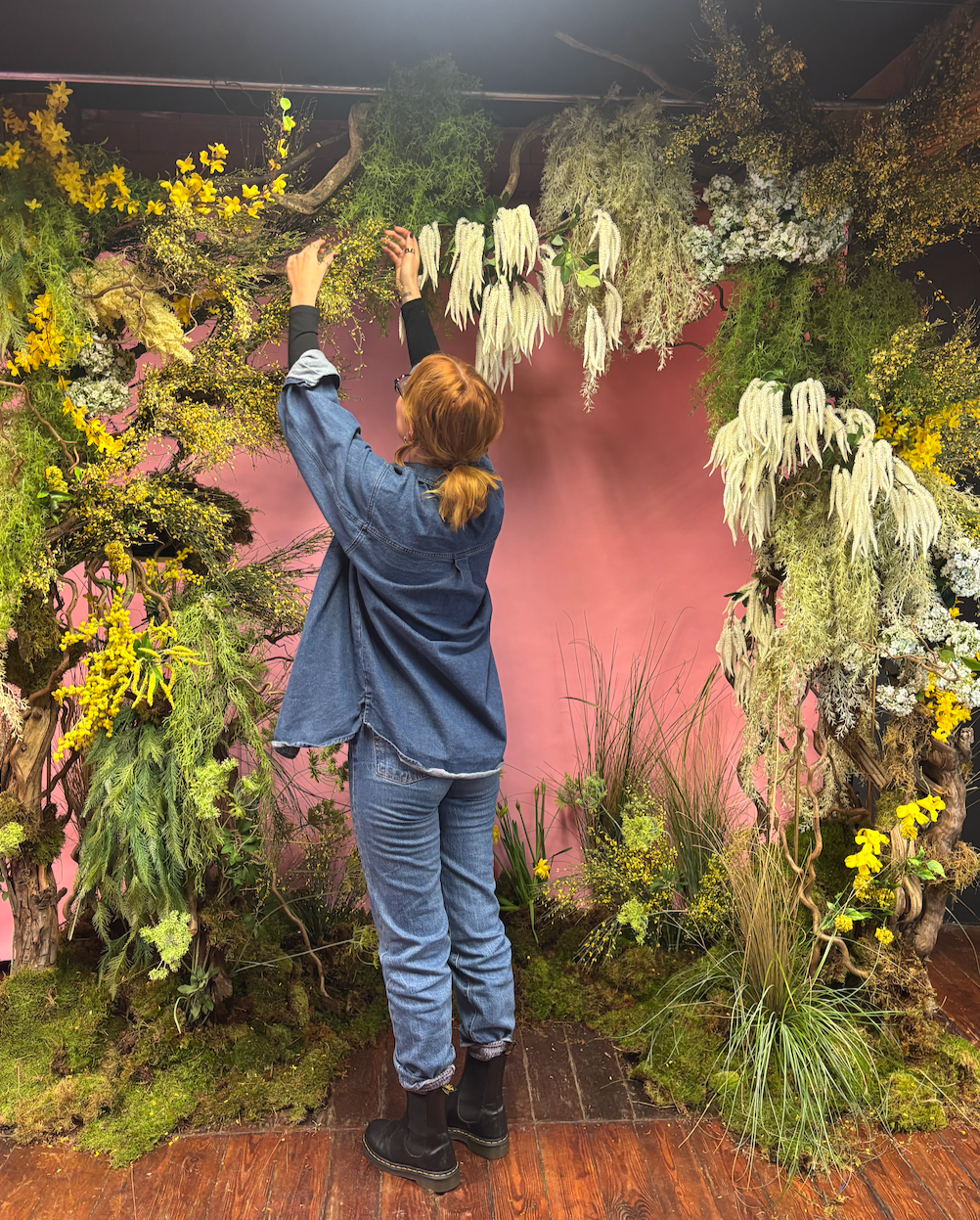 Student works on the final bits of the large scale floral installation. Materials used are fake and real flower, moss and grasses.