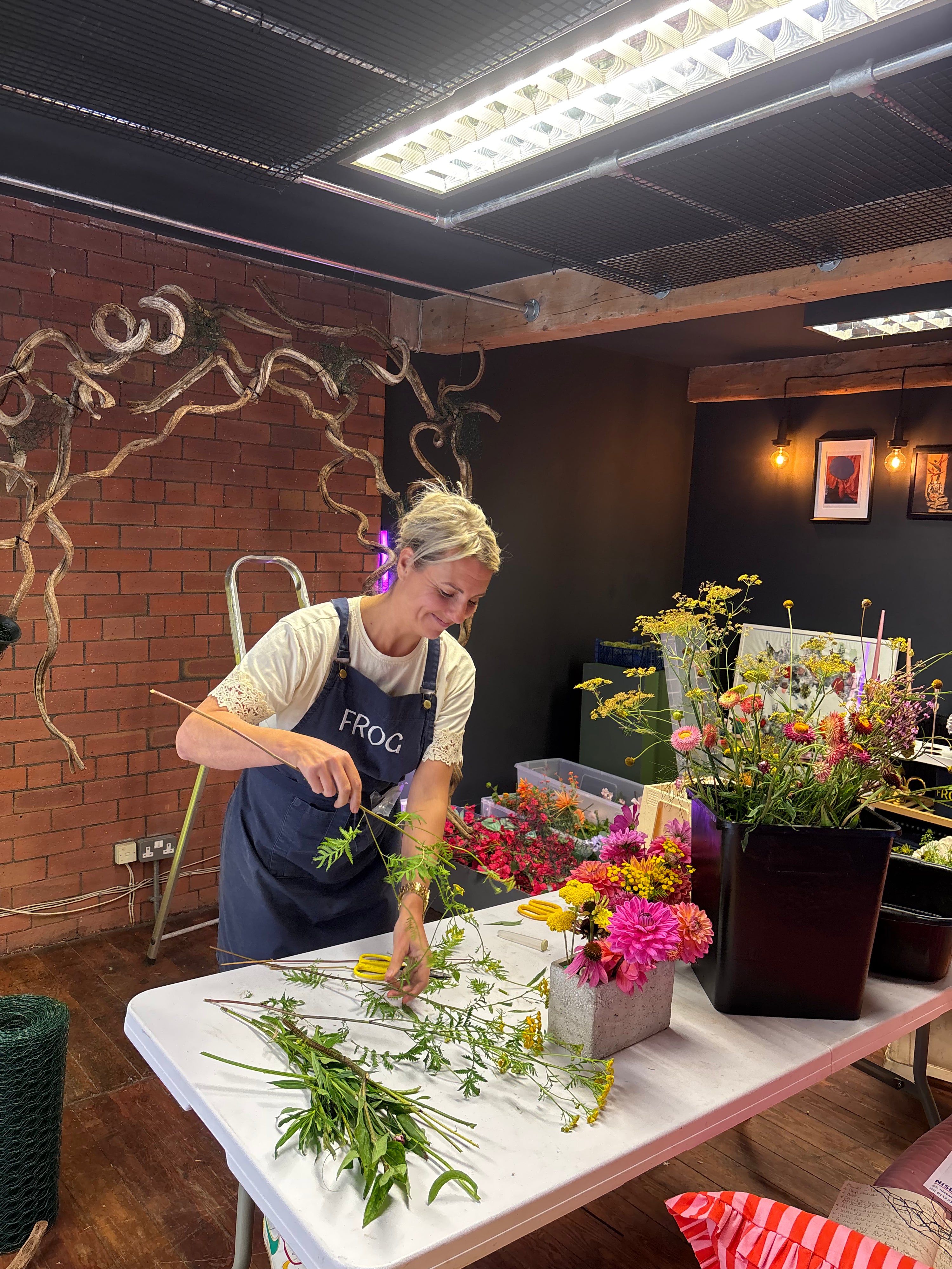 Woman arranging flowers in a workshop setting with tools and materials around.
