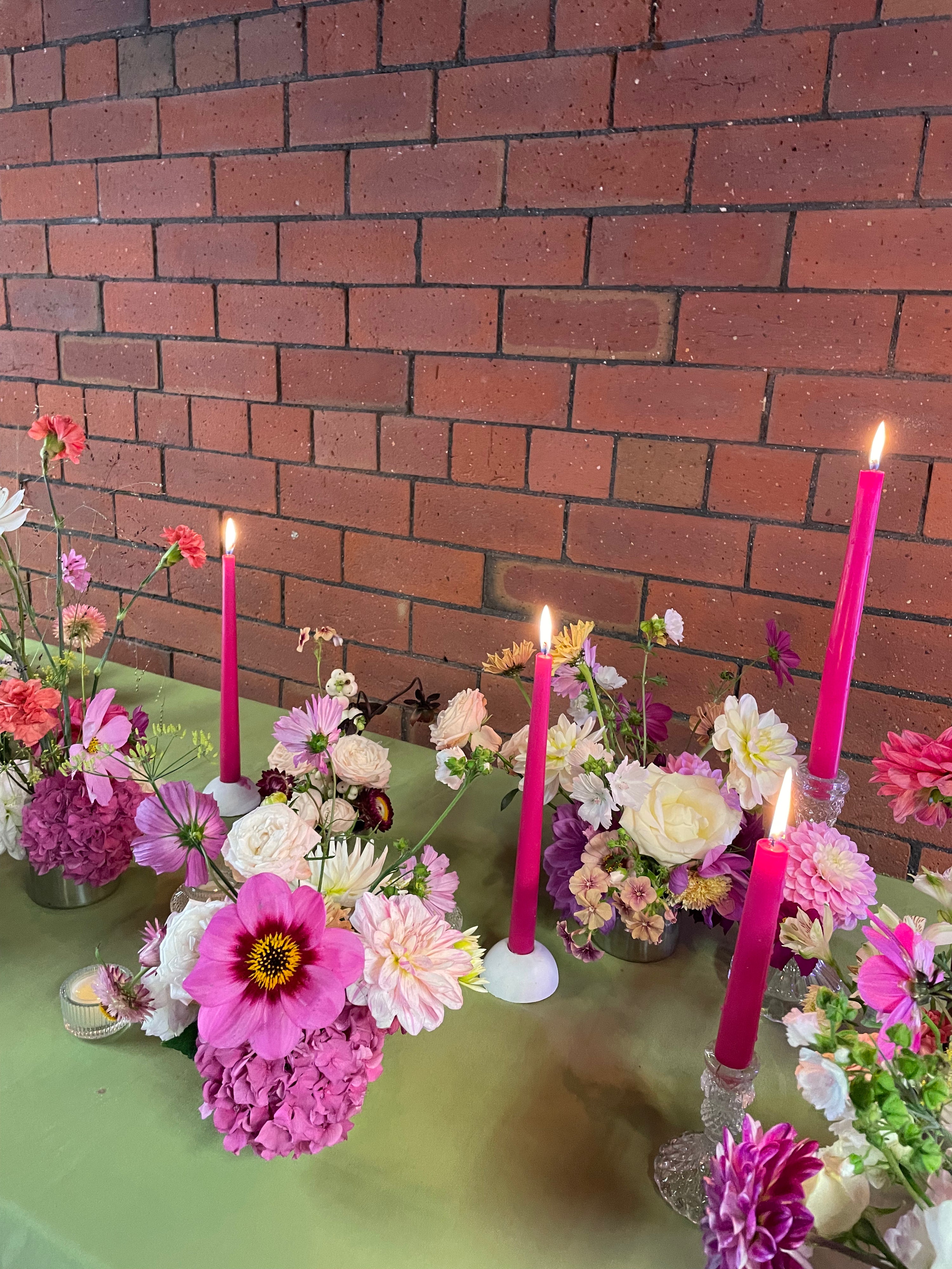 Decorative table setting with flowers and candles against a brick wall.