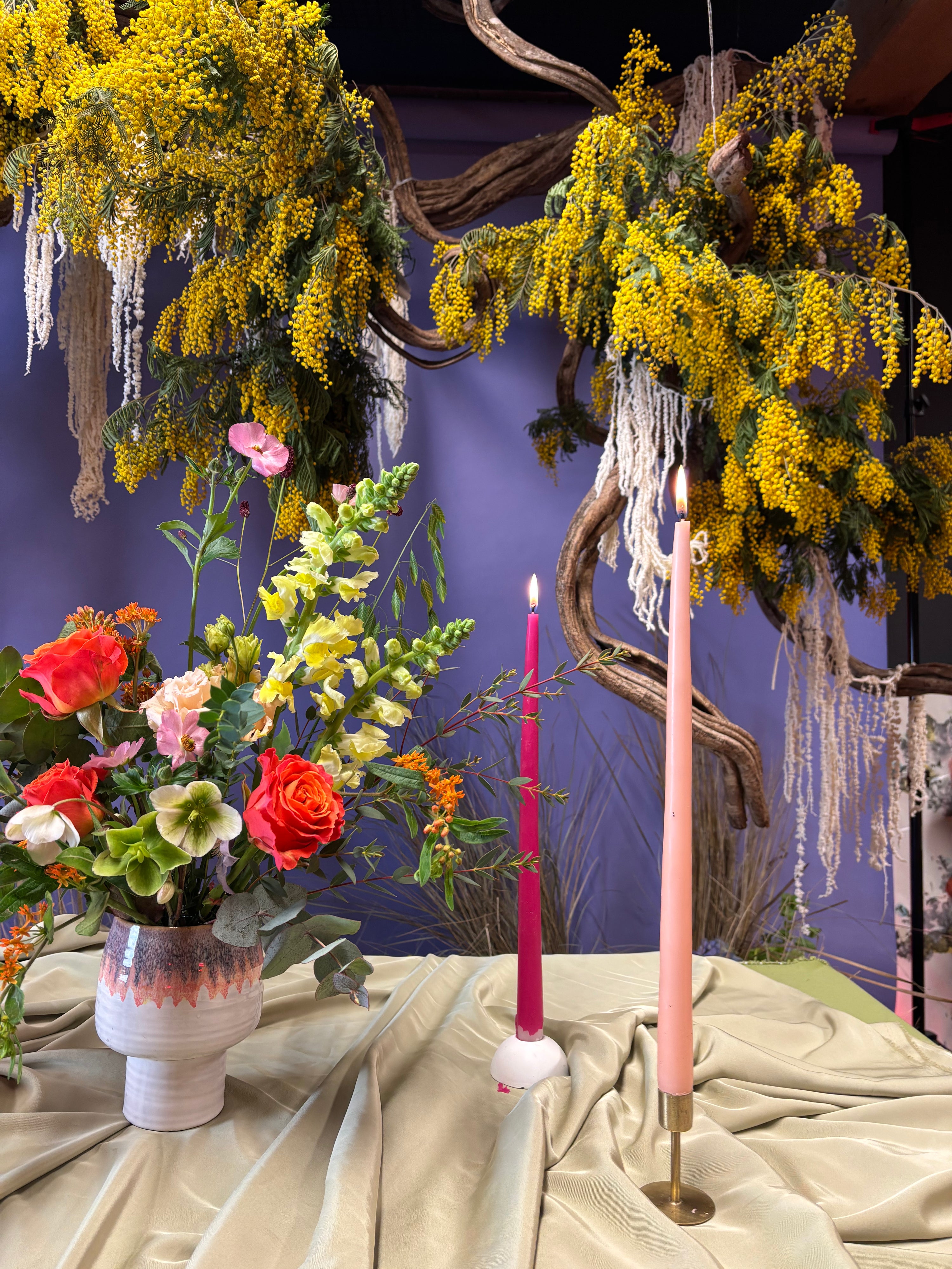 Decorative setup with flowers, candles, and hanging plants against a purple wall.