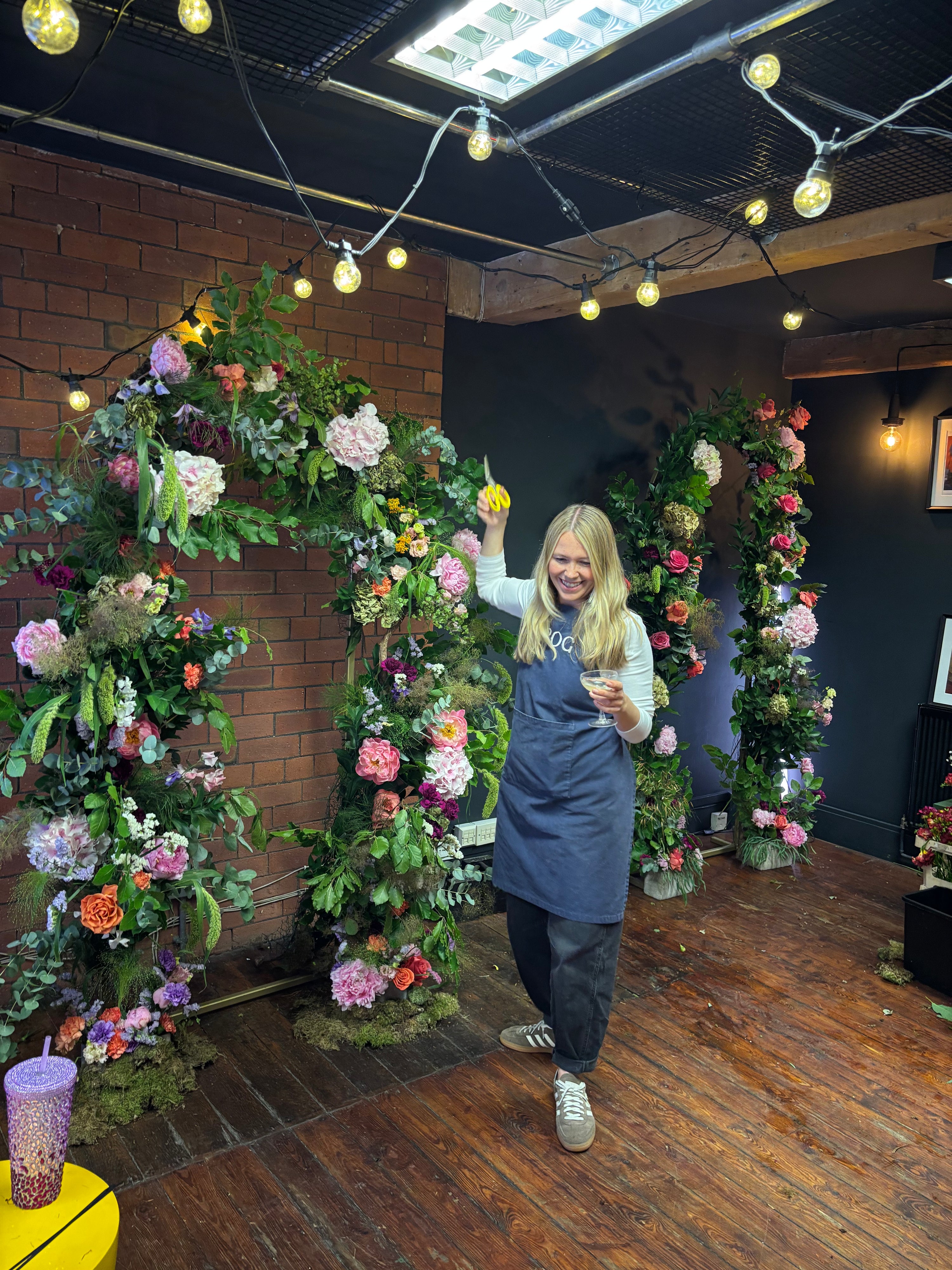 Woman standing among floral arches in a room with decorative lights.